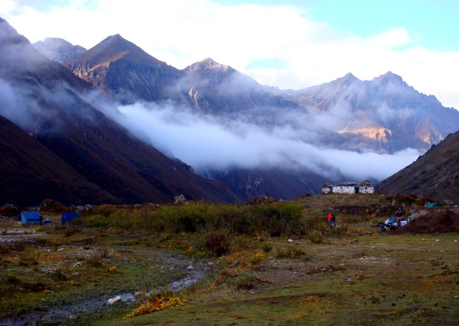 A trekking camp on an alpine meadow at dusk, with cloud pouring over the ridge behind