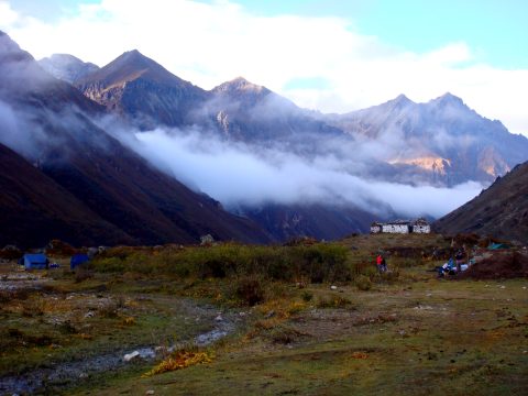 A trekking camp on an alpine meadow at dusk, with cloud pouring over the ridge behind