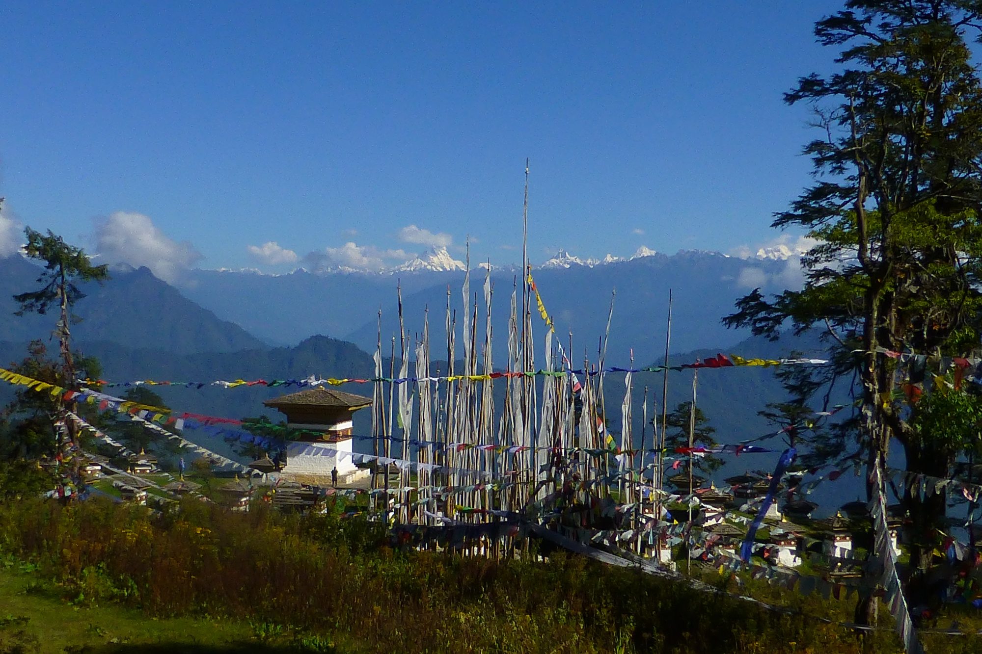 Prayer flag poles on a ridge with a small chorten and the snow peaks of the eastern Himalayas behind