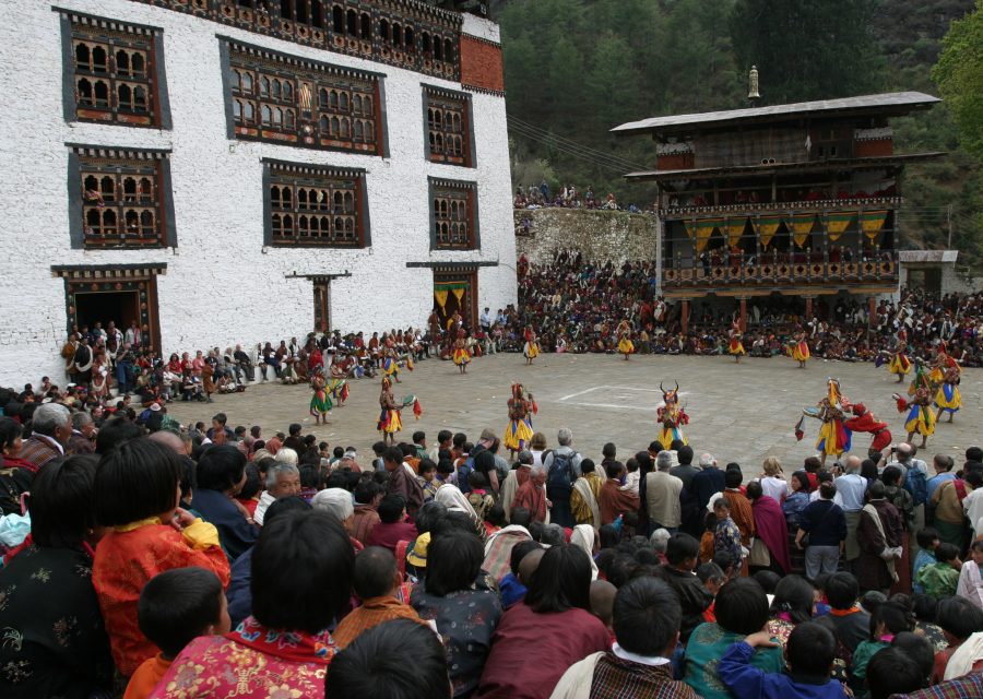 Masked dancers performing in a dzong courtyard before a seated crowd