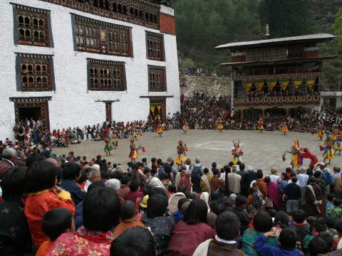 Masked dancers performing in a dzong courtyard before a seated crowd