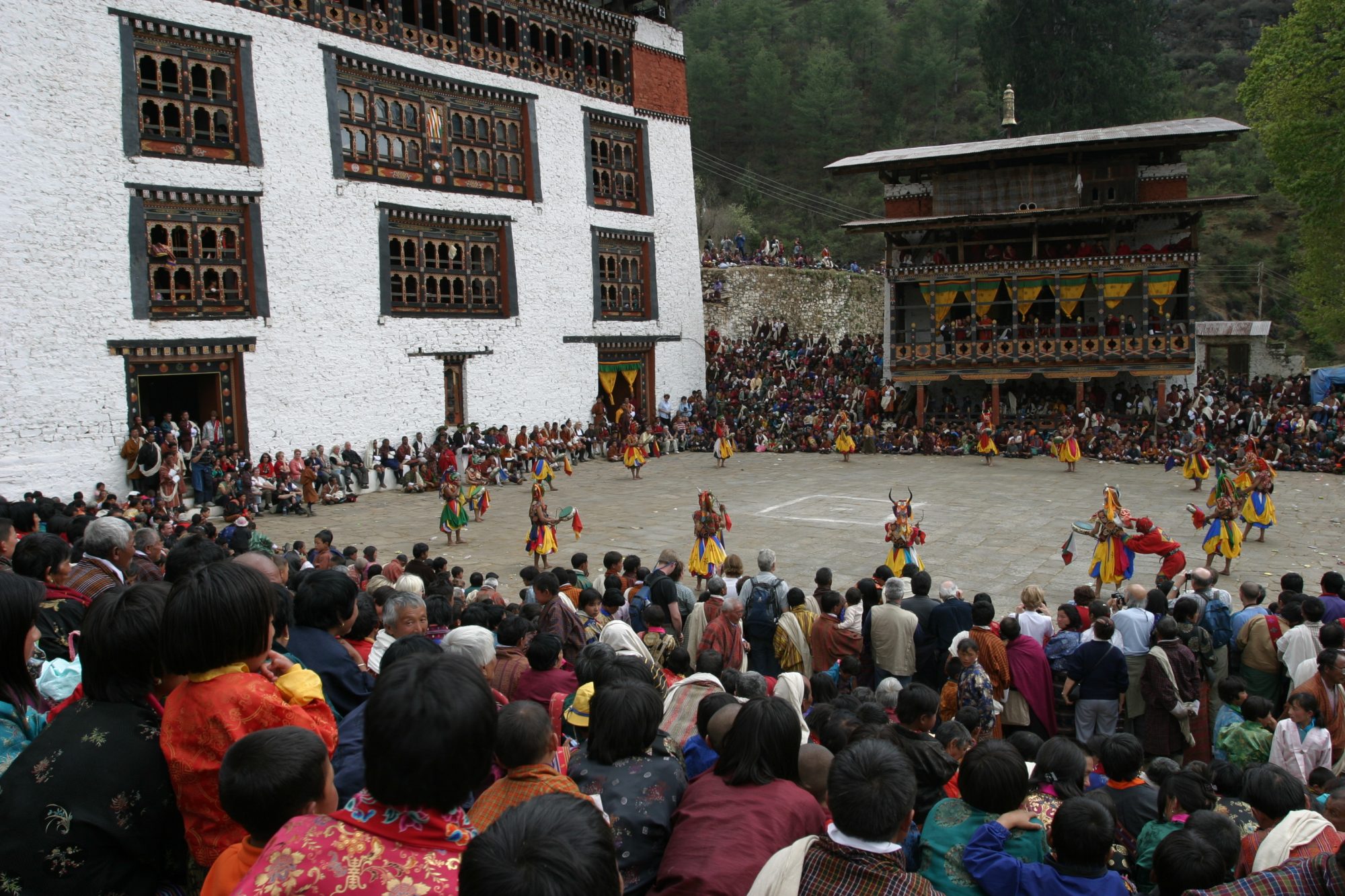 Masked dancers performing in a dzong courtyard before a seated crowd